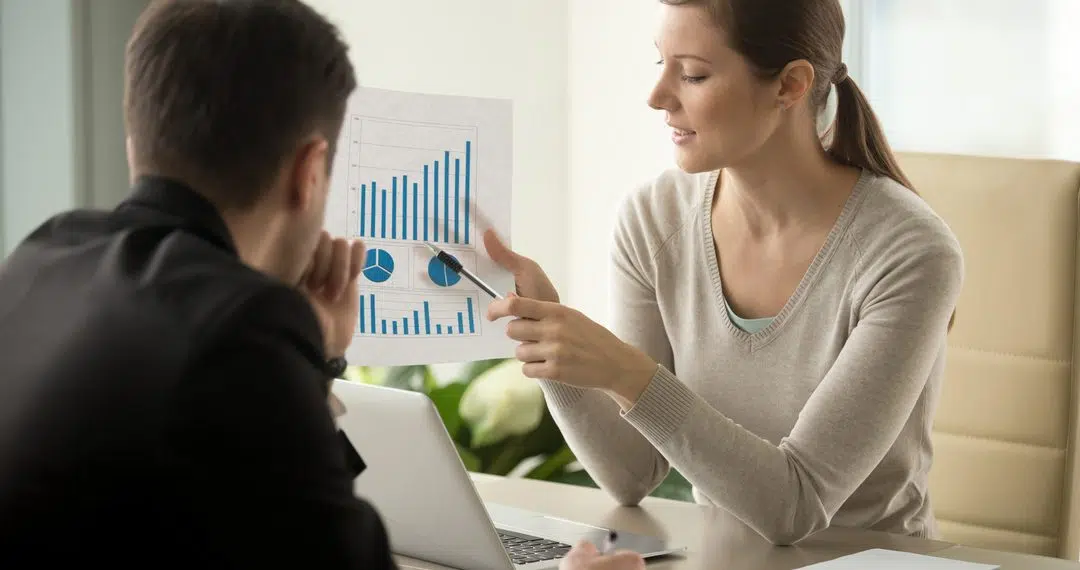 Attractive millennial businesswoman presenting company financial indicators, telling business partner about investment plan, showing document with project positive stats sitting at office desk