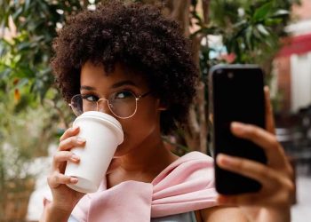 Tendencias de consumo mujer tomando café mientras revisa el celular