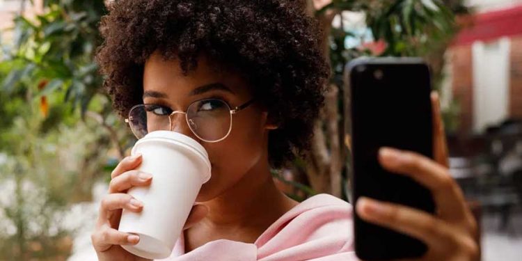 Tendencias de consumo mujer tomando café mientras revisa el celular