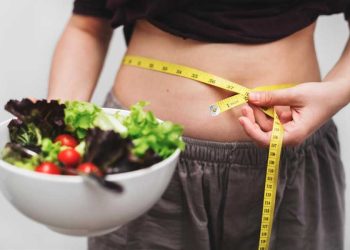 mujer midiendo su abdomen con comida saludable en un bowl