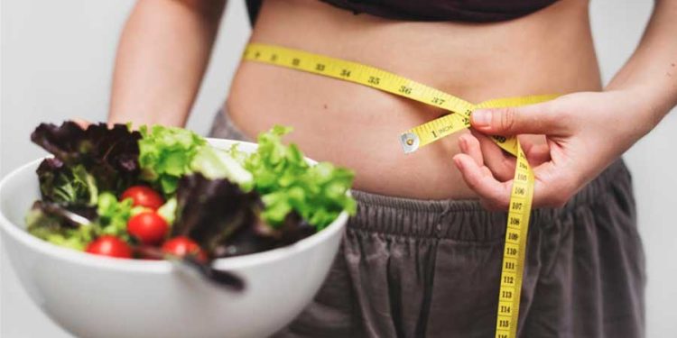 mujer midiendo su abdomen con comida saludable en un bowl